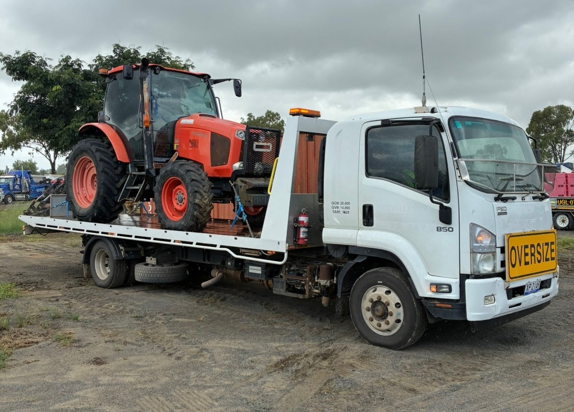 A small red tractor being transported on one of our tilt tray trucks
